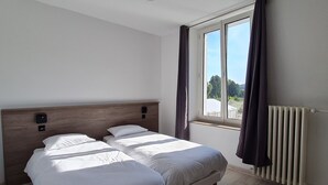 A hotel room with two single beds, a window with curtains, a radiator, and a view of the outdoors. - Bright 2-4 pers. loft with terrace and on-site restaurant (Lacroix-sur-Meuse)