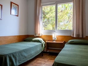 Ein Zimmer mit zwei Einzelbetten, einem Nachttisch mit Lampe, einem Fenster mit Vorhängen und einem an der Wand hängenden Bild.