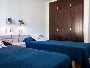 Et værelse med to senge, et natbord, en væglampe og en stor garderobe.