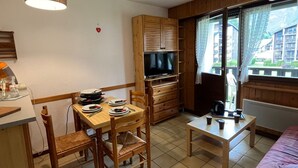 A compact room with a wooden dining table, chairs, a television, a small table with cups, and a window with curtains. - Cozy studio for 4, balcony, in Samoëns (Samoëns)