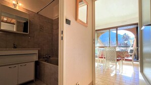 Un baño moderno con un espejo grande, una bañera y un lavamanos. Hay una puerta corrediza de vidrio que da a un balcón con mobiliario exterior.