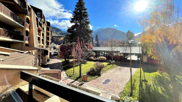 Un patio de hotel con una montaña de fondo, un árbol grande y un edificio con balcones.