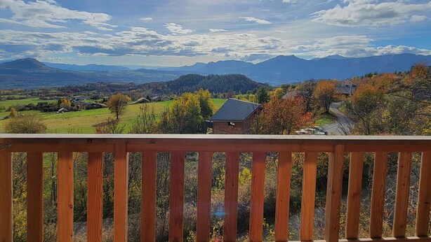 Blick vom hölzernen Balkon auf eine gebirgige Landschaft im Herbst, mit blauem Himmel und Bergen in der Ferne.