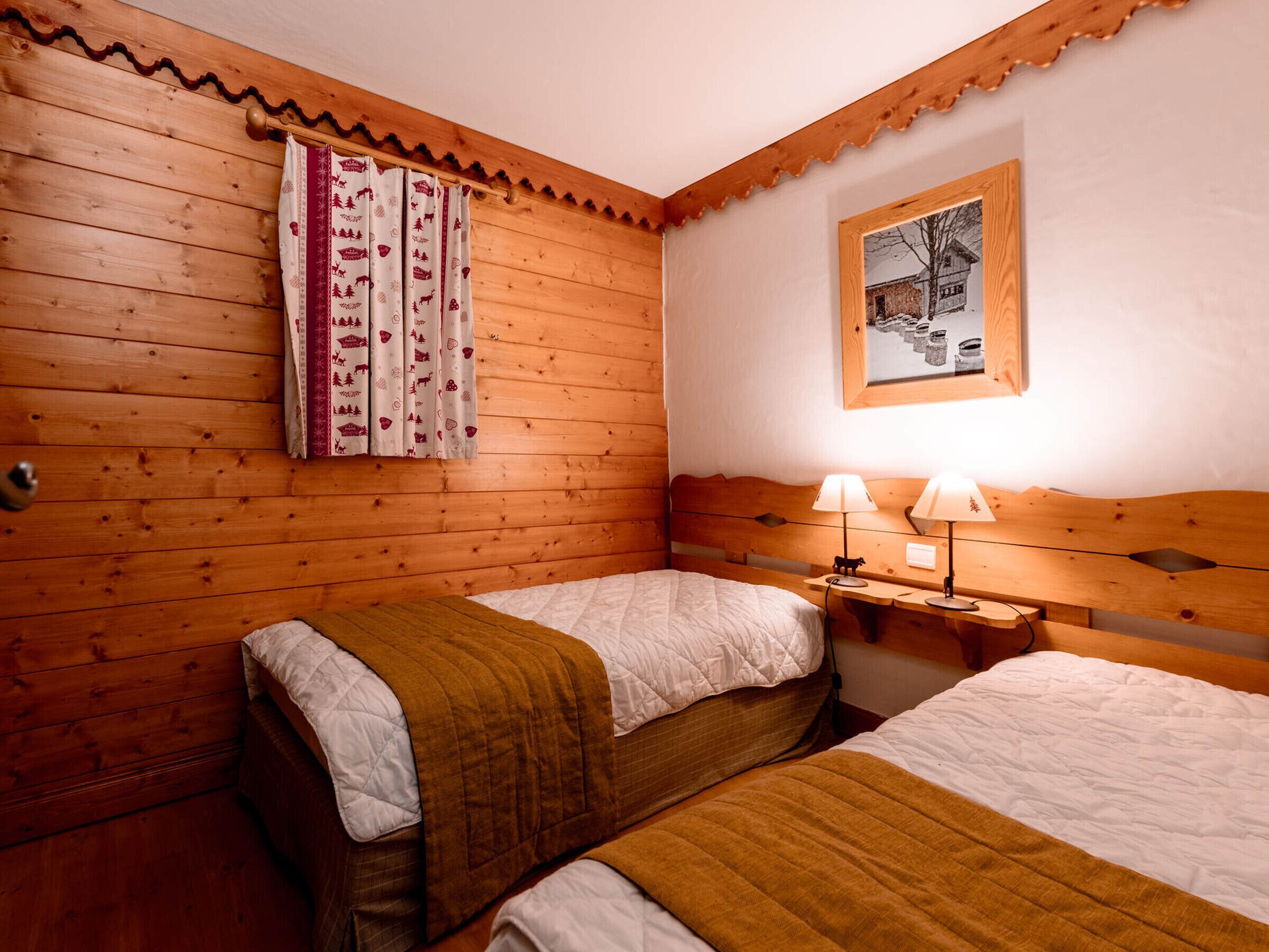 Una stanza in legno con due letti, un quadro appeso e una finestra con tende.