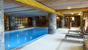 Una piscina interna con pilastri in pietra, travi in legno e pavimento piastrellato.