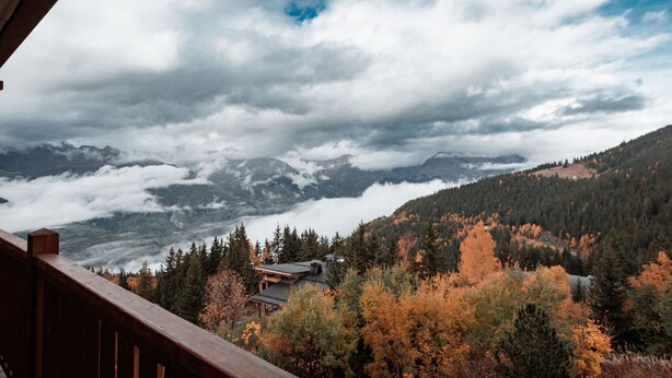 Paesaggio montano con foglie autunnali, un pontile di legno e vista su montagne lontane.
