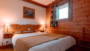 Una stanza accogliente in legno con un letto, due lampade da comodino, una finestra con tende a motivi e un quadro appeso al muro.