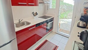 A modern kitchen with red cabinets, a stainless steel sink, a built-in oven, and a sliding glass door leading to an outdoor area.