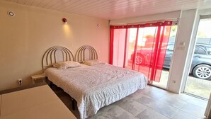A bedroom with a bed, a bench, a door, and a view of the outside.