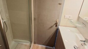 A bathroom with a glass shower enclosure, a wooden vanity, and a white sink.