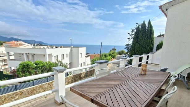 A wooden deck with a table and chairs, overlooking a residential area and the sea.