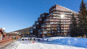 A multi-story hotel with balconies, a ski slope in the foreground, and a mountainous backdrop. - Ski-in studio with balcony, sleeps 4 (Les Arcs 1800)