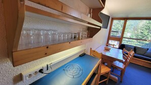 A wooden-framed kitchen with a blue countertop, a dining area with a table and chairs, and a window with a view of trees. - Ski-in studio with balcony, sleeps 4 (Les Arcs 1800)