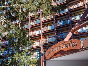 A multi-story building with balconies, a sign reading "Les Belles Challes," and surrounding trees.