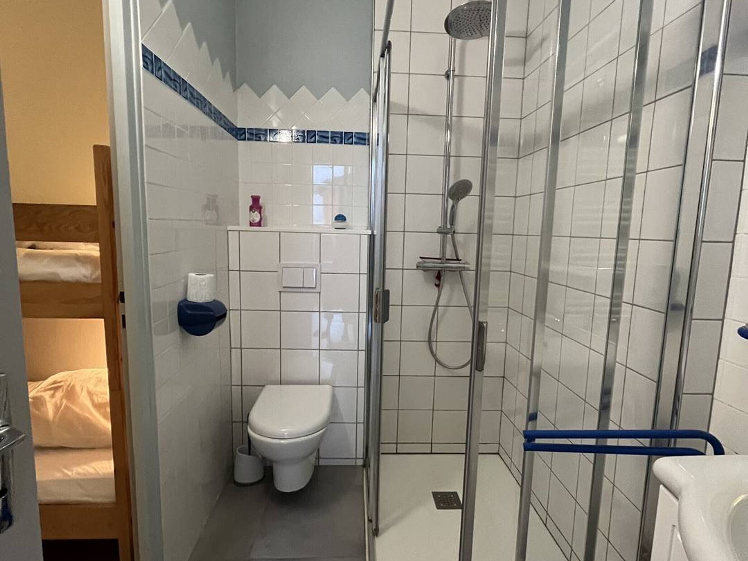 A compact bathroom with a toilet, shower, and a small shelf with toiletries.