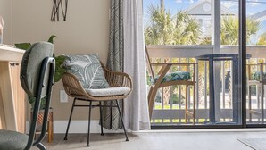 Una habitación con un ventanal grande, una silla de mimbre, un banco acolchado y vistas a un balcón con mobiliario exterior.