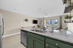 A modern kitchen with green cabinets, a granite countertop, and a built-in dishwasher.
