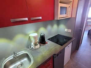 Une cuisine avec des meubles de rangement rouges, un évier en acier inoxydable, une machine à café et une plaque de cuisson à induction.