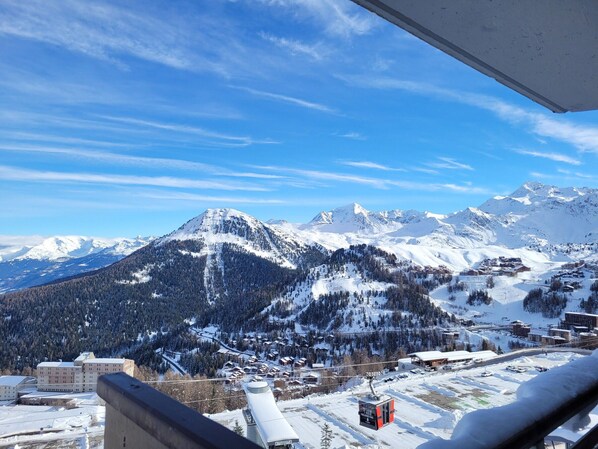 Un paysage de montagne enneigé, avec un télésiège et des bâtiments au premier plan.