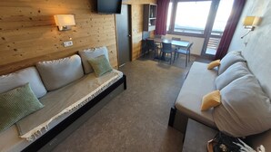 Una habitación acogedora con sofá, mesa de comedor y televisor montado en la pared.