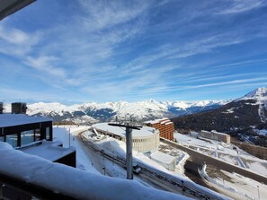 Een berglandschap bedekt met sneeuw, heldere lucht, een weg en gebouwen op de voorgrond.