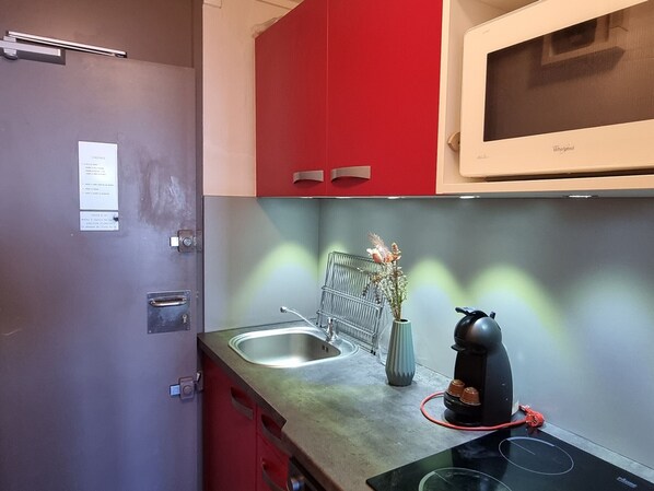 Een kleine keuken met een magnetron, waterkoker en spoelbak.
