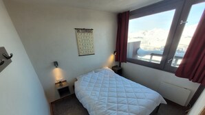 Un dormitorio con cama, un cartel sobre técnicas de esquí en la pared, una ventana con vistas a montañas y un radiador.