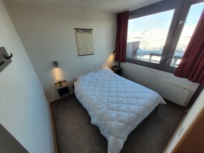 Un dormitorio con cama, un cartel sobre técnicas de esquí en la pared, una ventana con vistas a montañas y un radiador.