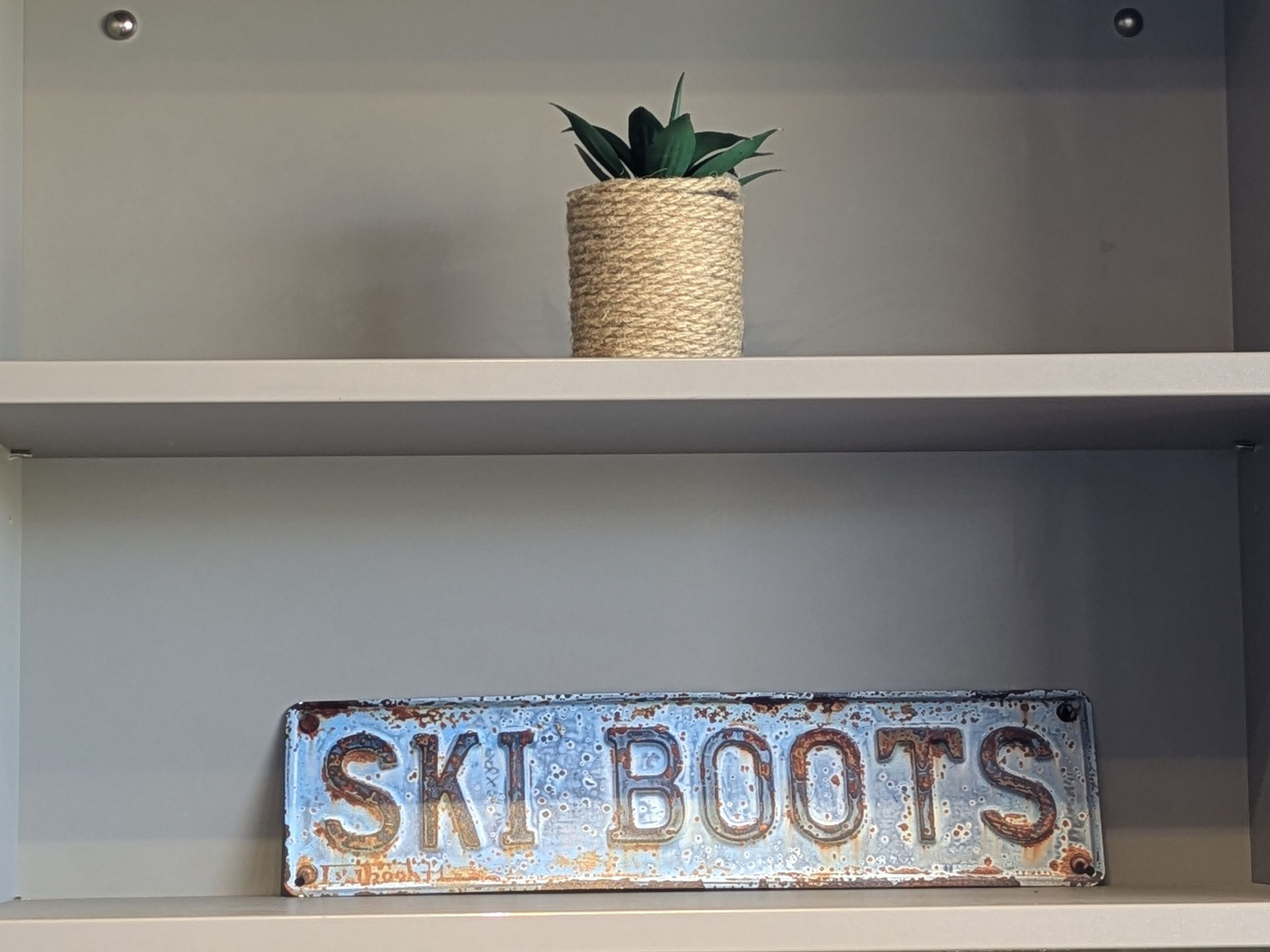 En hylde med en plante og et skilt, der står 'SKI BOOTS'.