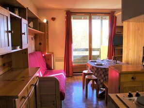 A cozy room with a bed, a table with chairs, a kitchen area, and a sliding glass door leading to an outdoor area. - Sunny Studio with Mountain View, 300m from Slopes, Sleeps 4, Vars Sainte Marie (Vars-Sainte-Marie)