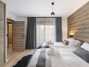 A hotel room with two beds, a wooden wall, a window with curtains, and a hanging light fixture.