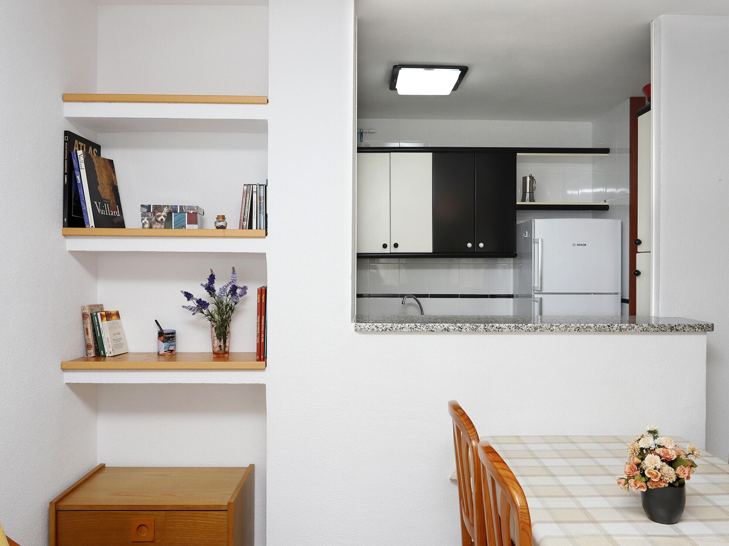 A compact kitchen with white cabinets, a Bosch refrigerator, and a small dining area with a wooden table and chairs.
