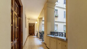 Un pasillo estrecho con puertas de madera, suelo de baldosas y una ventana con balcón.