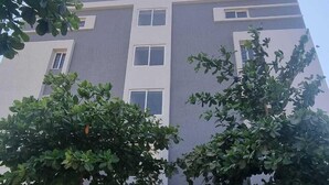 A multi-story building with a modern architectural design, featuring a central entrance with a decorative gate, surrounded by lush greenery. - PPH Living KVR Residency (Tada)