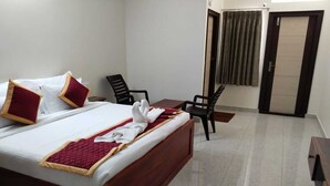 A hotel room with a bed, two chairs, a small table, and a door with curtains. - PPH Living KVR Residency (Tada)