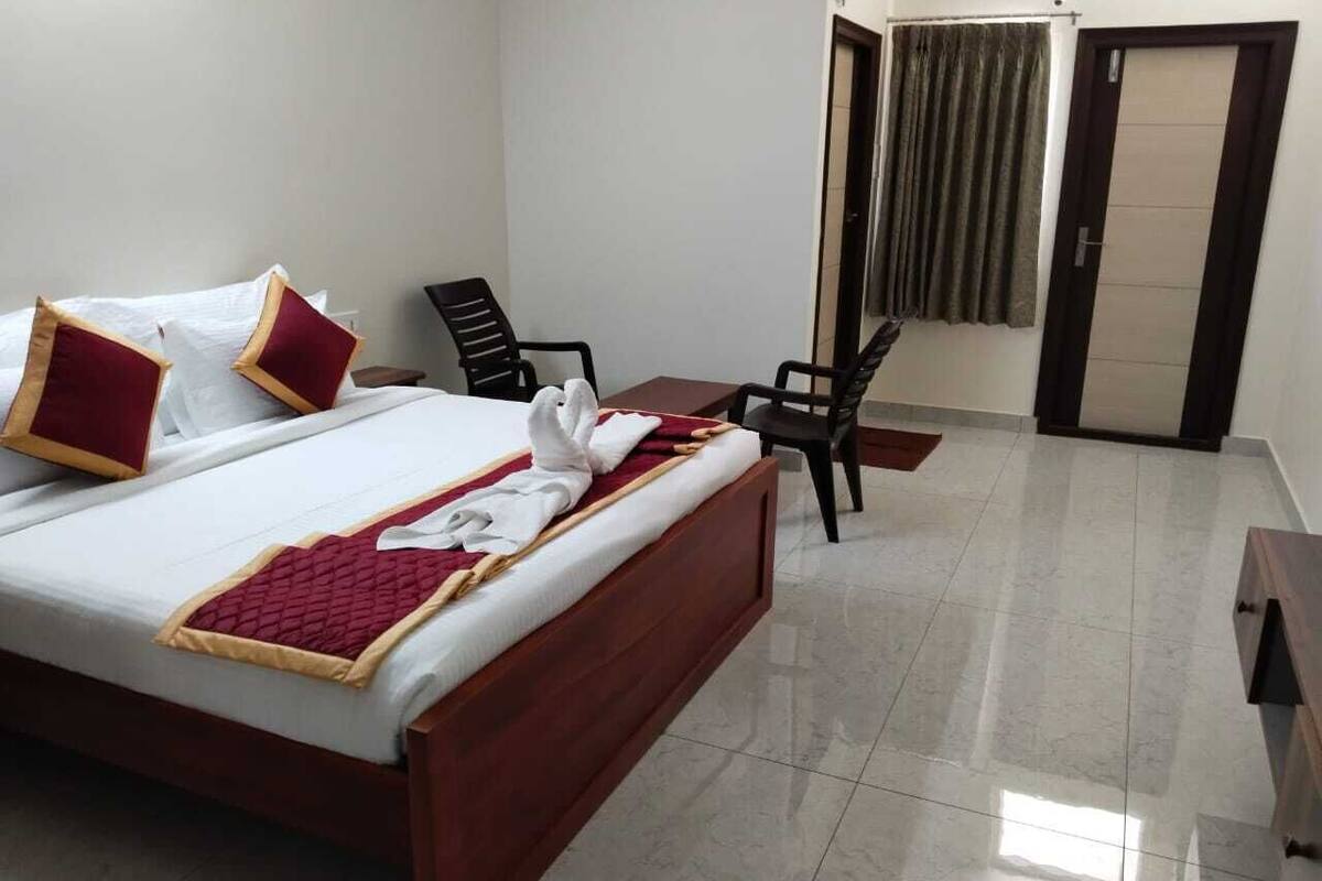 A hotel room with a bed, two chairs, a small table, and a door with curtains.