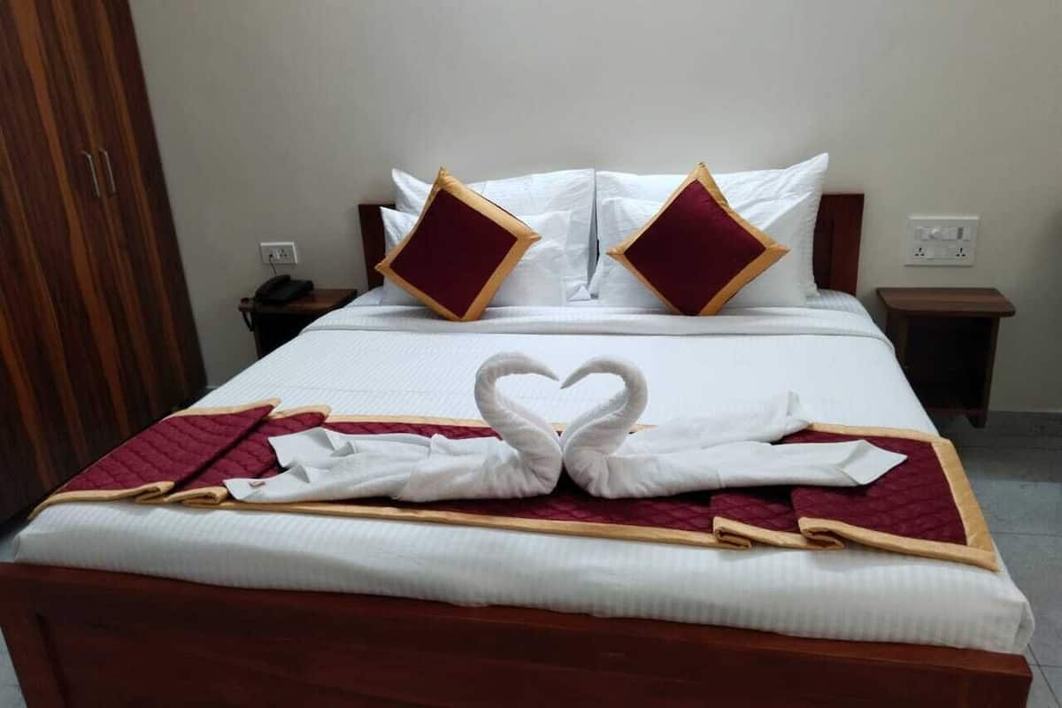 A neatly made bed with a heart-shaped towel arrangement, a wooden headboard, and a bedside table with a phone and a power outlet.