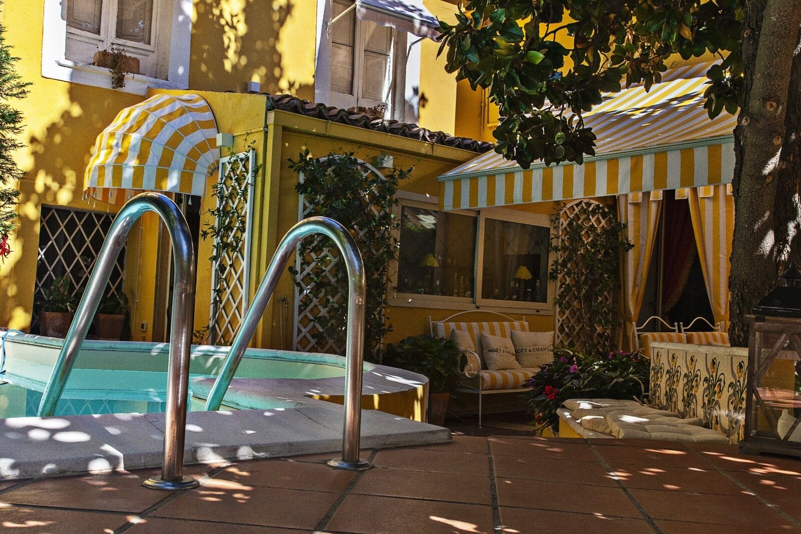 Zona de piscina con dos escaleras de metal, una tumbona y un toldo a rayas.