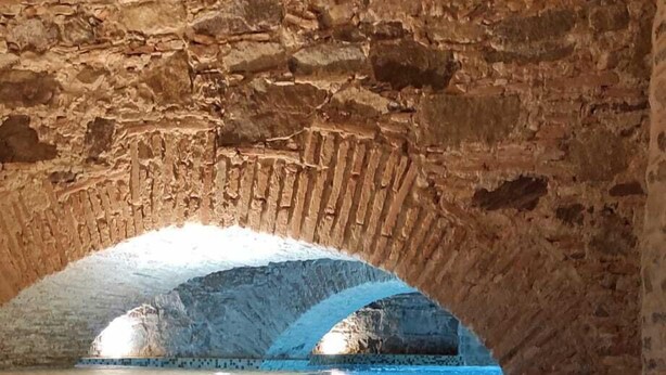 Une piscine intérieure dont le sol et les murs sont recouverts de carrelage, et qui est entourée de murs en pierre.