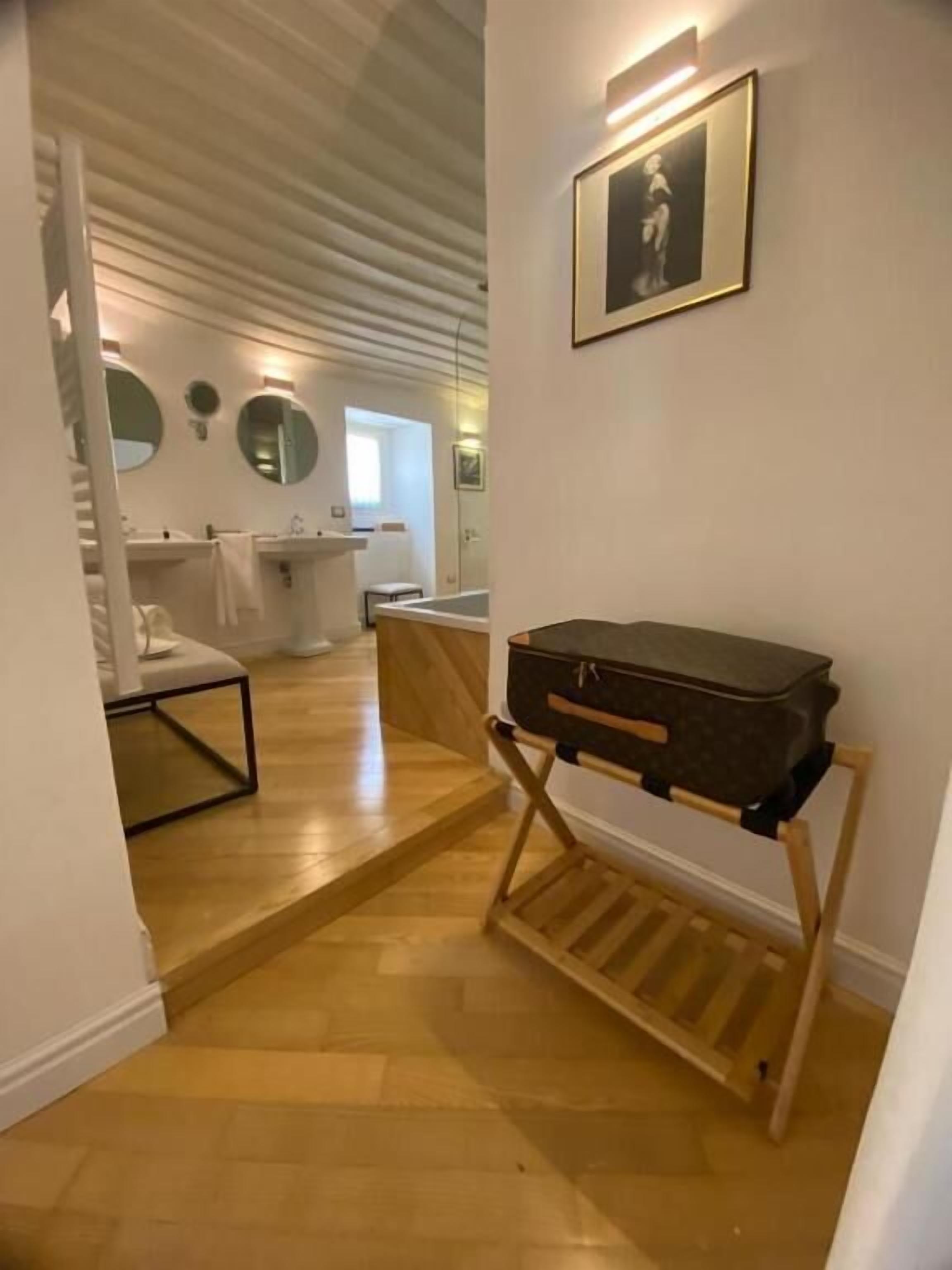 Une chambre d’hôtel avec un plancher en bois, un lit, une table de chevet, une valise posée sur un présentoir et un tableau encadré accroché au mur.
