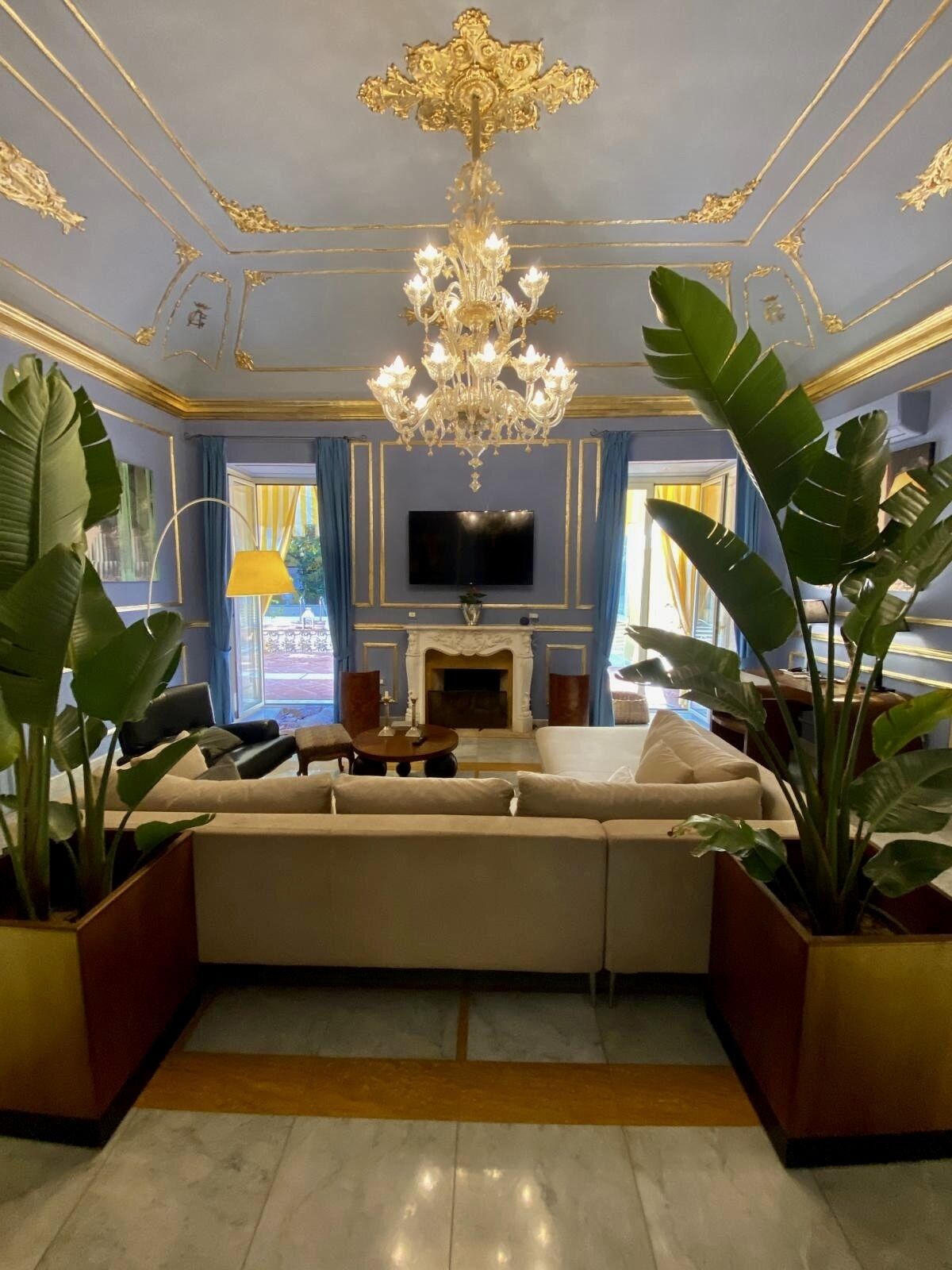 Una sala de estar lujosa con un sofá grande, una chimenea, un candelabro y plantas en macetas grandes.