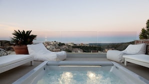 Un espace piscine aménagé sur le toit, avec deux chaises longues blanches et un jacuzzi, offrant une vue sur le paysage urbain.