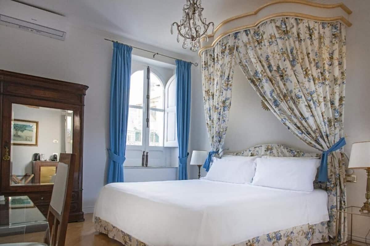 Ein Schlafzimmer mit Himmelbett, einer Chandelierleuchtre und Blick auf die Stadt durch das Fenster.