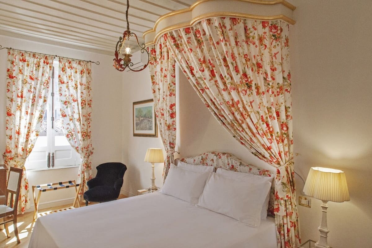 Ein Schlafzimmer mit einem Himmelbett, floralen Vorhängen, einer Chandelier und einem Schreibtisch mit Lampe.