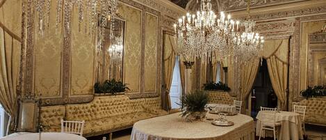 A grand dining room with ornate chandeliers, plush seating, and a classic interior design.