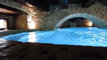 Una piscina interna con pareti in pietra, pavimento piastrellato e un arco in pietra.