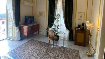 Una habitación amplia con una cama grande, una araña de cristal, un escritorio de madera, una silla y una planta en maceta.