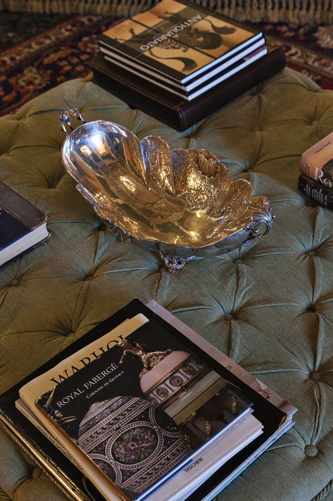 En plysset grøn sofa med en dekorativ sølvskål og en bog med titlen "Royal Fabergé".