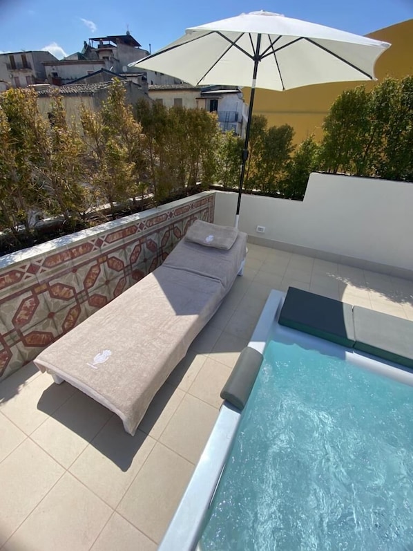 Zona de piscina en la azotea con una silla de descanso y una sombrilla.