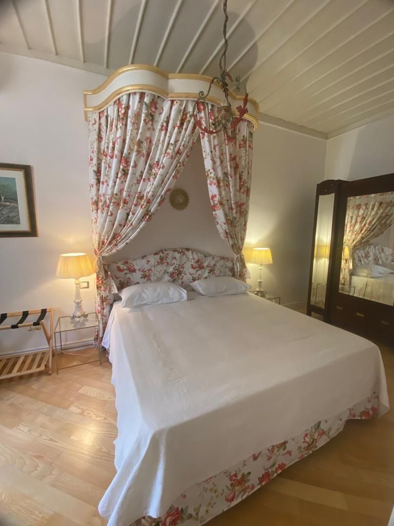 A bedroom with a canopy bed, bedside lamps, a wooden bench, and a mirror.